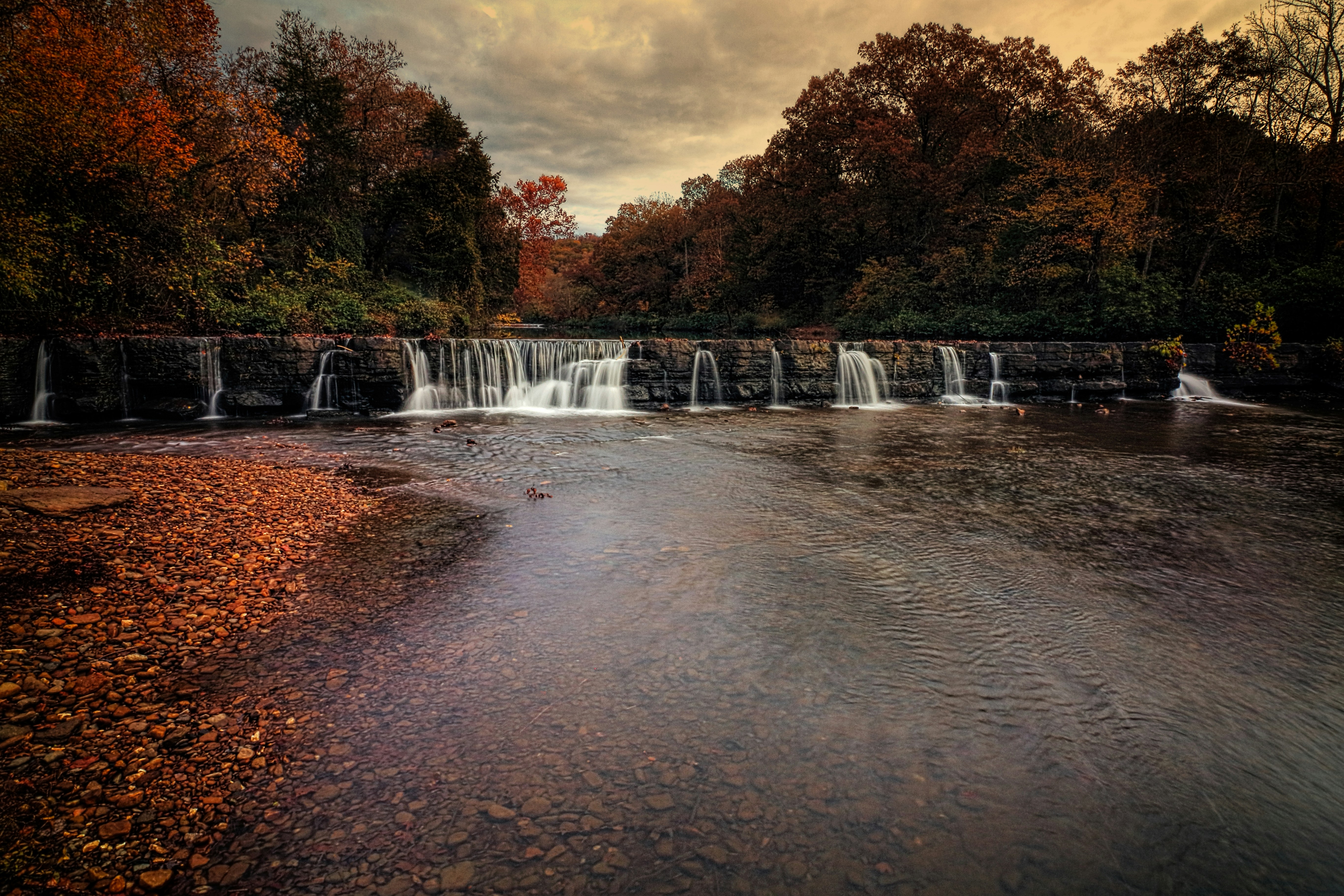 Wide waterfall flowing over a rock ledge surrounded by autumn forest in Arkansas
